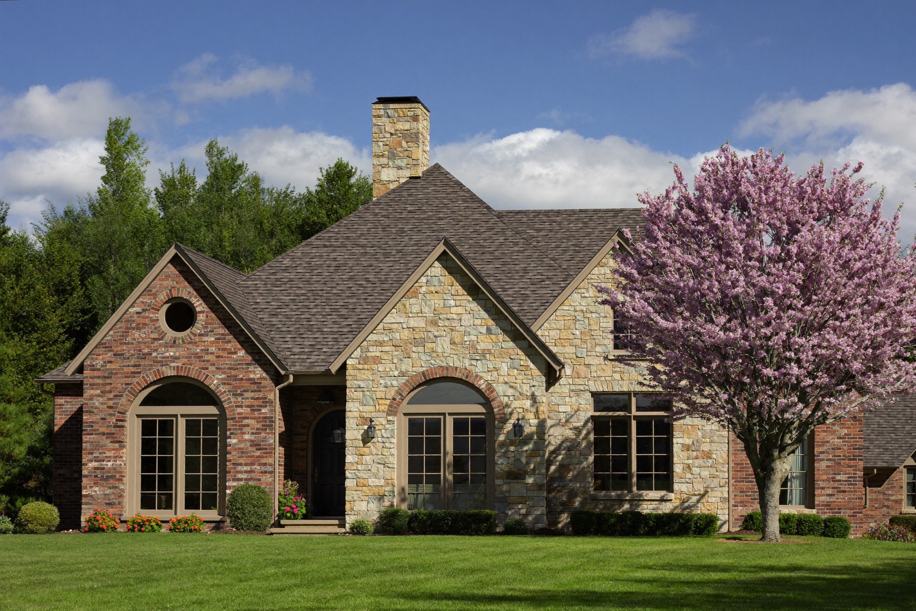 A brick Tulsa home with a new architectural shingle roof and a blooming redbud tree in the yard