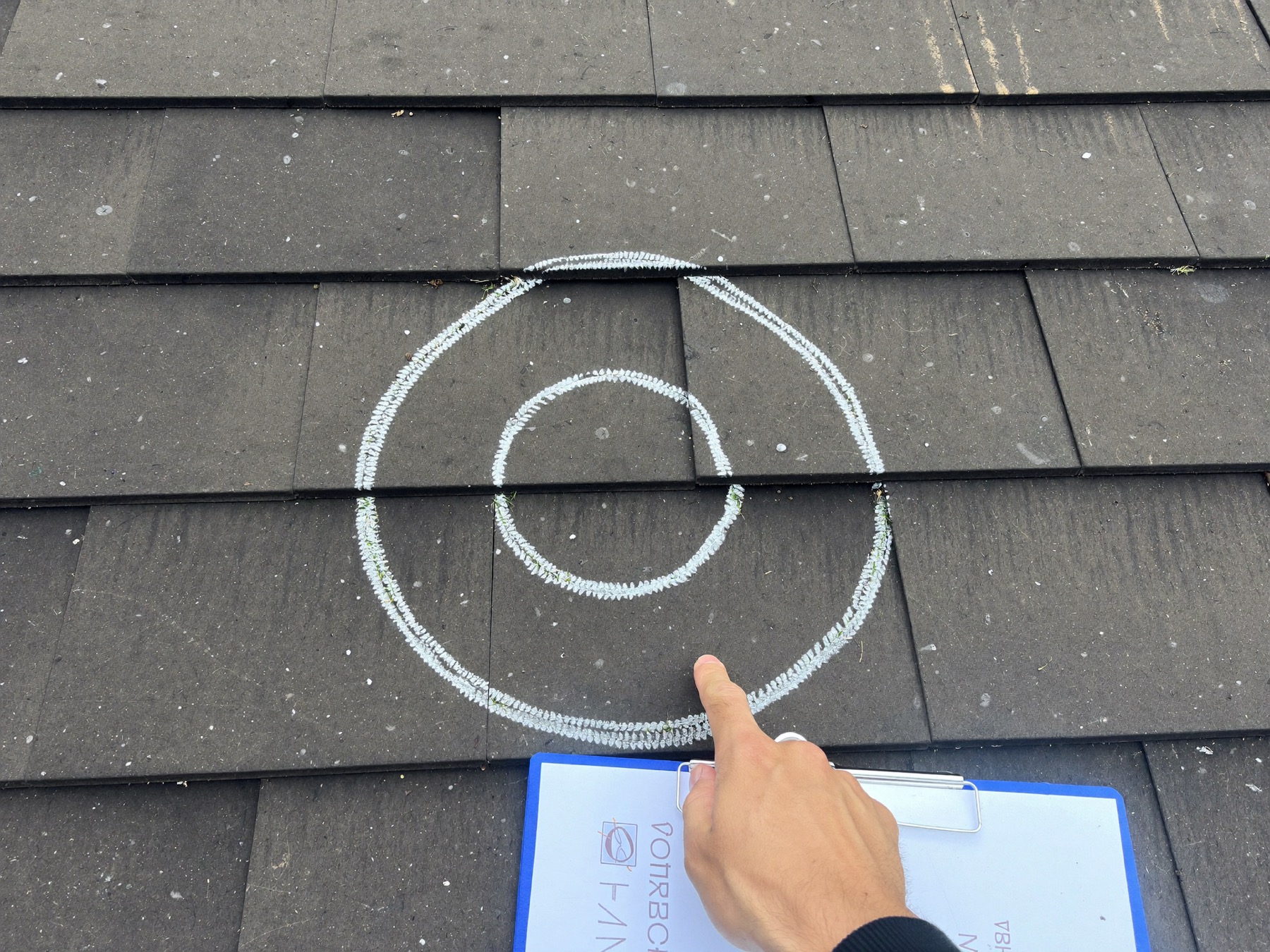 A Redbud inspector pointing at chalk-circled hail impact marks on shingles